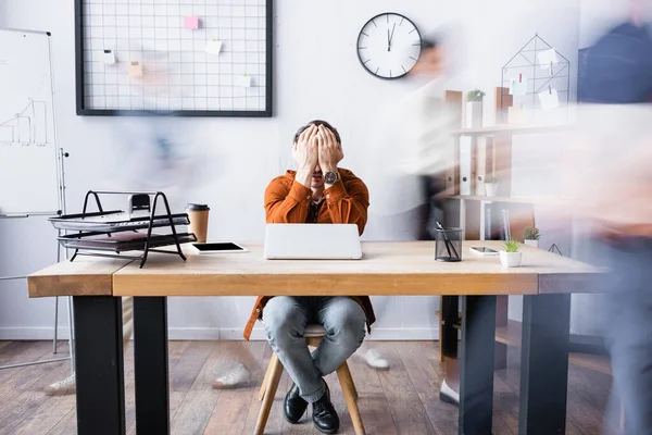 Uomo d'affari esausto che copre il viso con le mani mentre si siede sul posto di lavoro in ufficio open space, banner, movimento sfocatura — Foto stock