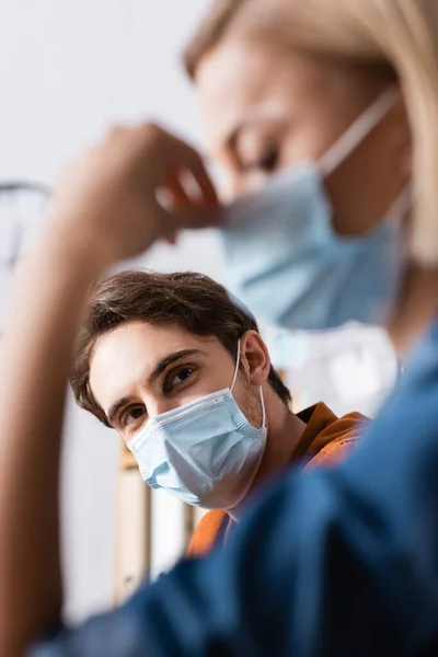 Young businessman in protective mask looking at colleague on blurred foreground — Stock Photo