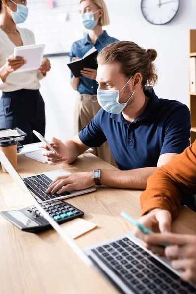 Equipo joven de empresarios multiculturales en máscaras médicas trabajando juntos en oficinas de espacio abierto - foto de stock