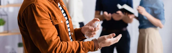 Partial view of manager spraying sanitizer on hands near businesspeople on blurred background, banner — Stock Photo