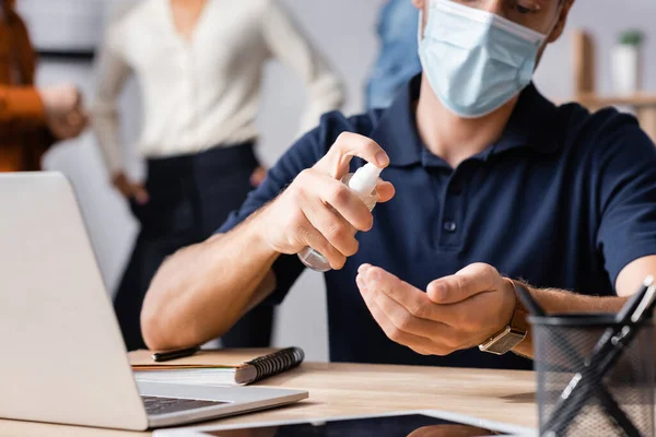 Partial view of manager using sanitizer while colleagues standing on blurred background — Stock Photo