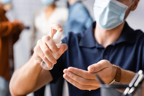 Cropped view of businessman spraying antiseptic on hands near colleagues on blurred background — Stock Photo