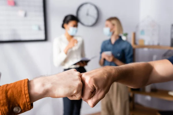 Two businessmen doing fist bump near multicultural businesswomen talking on blurred background — Stock Photo
