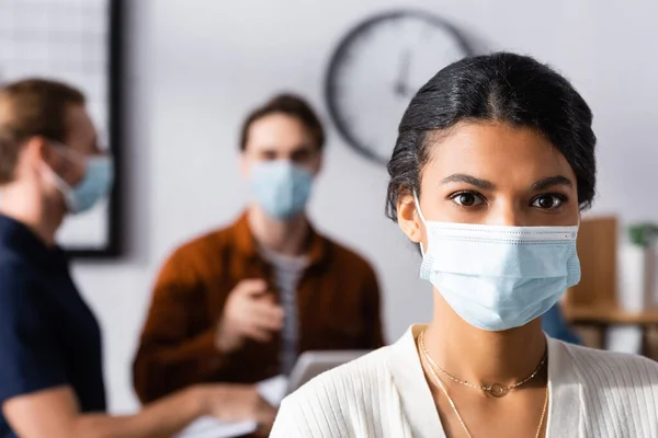 African american businesswoman in protective mask looking at camera near managers on blurred background — Stock Photo