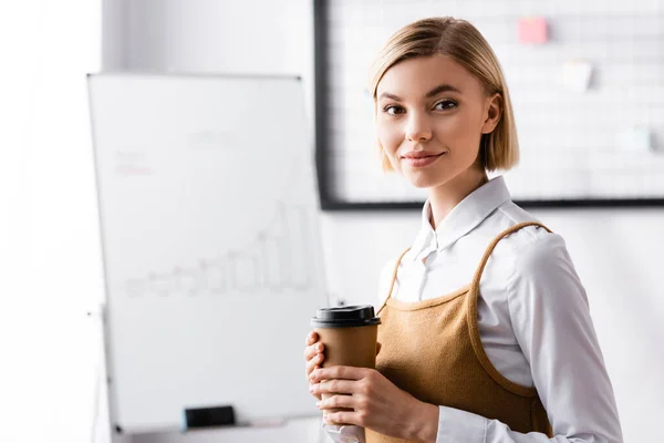 Happy businesswoman looking at camera while holding coffee to go — Stock Photo