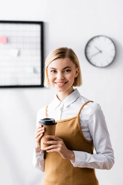 Fröhliche Geschäftsfrau mit Kaffee to go während sie in die Kamera lächelt — Stockfoto