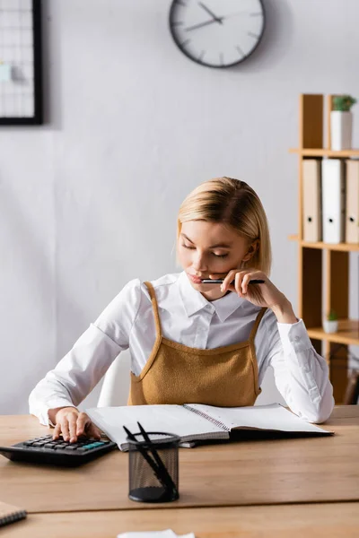 Comptable sérieux à l'aide d'une calculatrice près d'un ordinateur portable au premier plan flou — Photo de stock