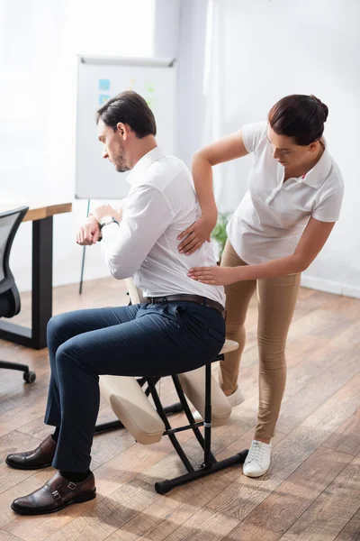 Massagista fazendo massagem sentada de empresário de volta ao escritório em fundo turvo — Fotografia de Stock