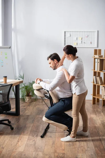 Massaggiatrice donna massaggiatrice collo massaggiante di uomo d'affari seduto sulla sedia di massaggio in ufficio — Foto stock