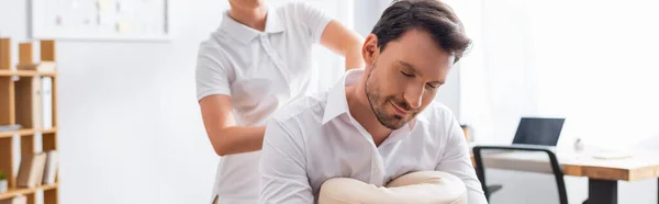 Masseurin massiert Rücken einer lächelnden Kundin mit geschlossenen Augen im Büro auf verschwommenem Hintergrund, Banner — Stockfoto