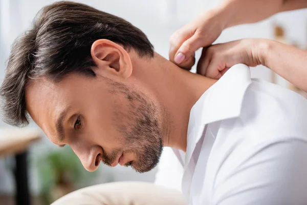 Vista de cerca de masajista masajista masajeando cuello de hombre de negocios barbudo sobre fondo borroso - foto de stock