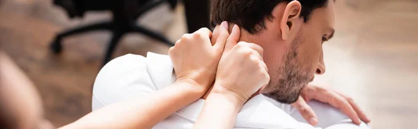 Massagetherapeutin mit ausgestreckten Händen, die den Nacken eines Geschäftsmannes auf verschwommenem Vordergrund massieren, Banner — Stockfoto