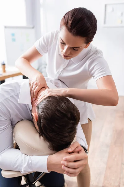 Masseuse doing seated massage of businessman neck in office on blurred background — Stock Photo