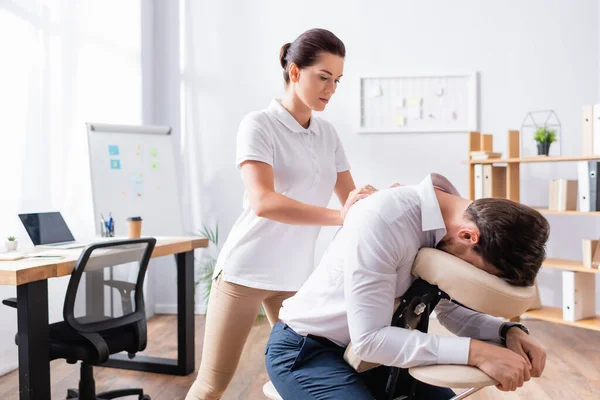 Masseuse doing seated massage of businessman back in office — Stock Photo