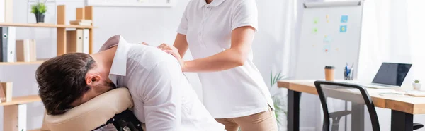 Жіночий масажист масажує спину бізнесмена, сидячи на масажному кріслі в офісі, банер — стокове фото