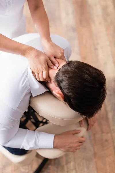Vista aérea de masajista haciendo masaje sentado del cuello del cliente - foto de stock