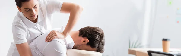 Позитивний масажист робить масаж рук для клієнта в офісі на розмитому фоні, банер — стокове фото