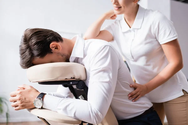 Massagem massagista sorridente de volta de empresário com cotovelo no escritório em fundo borrado — Fotografia de Stock