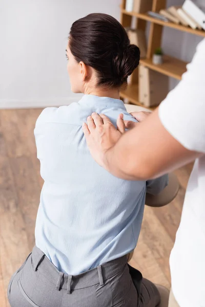 Massagem terapeuta fazendo massagem sentada de ombro empresária em primeiro plano desfocado — Fotografia de Stock