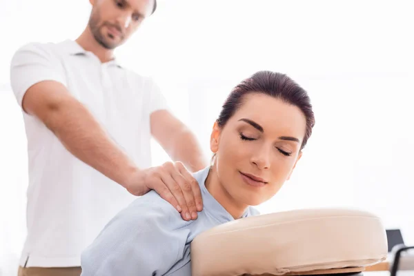 Focused masseur doing shoulders massage of positive businesswoman with closed eye on blurred background — Stock Photo