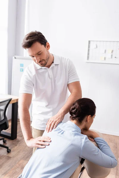 Lächelnder Massagetherapeut massiert Rücken einer Geschäftsfrau auf Massagesessel im Büro — Stock Photo