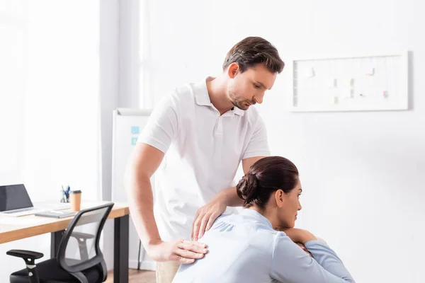 Massaggiatore concentrato guardando la donna bruna, mentre fa un massaggio alla schiena in ufficio — Foto stock