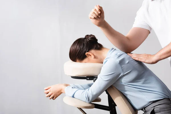Vista lateral de masajista mujer masaje espalda con codo, sentado en silla de masaje sobre fondo blanco - foto de stock