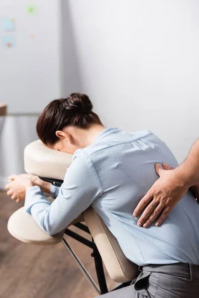 Masseur tut sitzende Rückenmassage für weibliche Klientin auf verschwommenem Hintergrund — Stockfoto