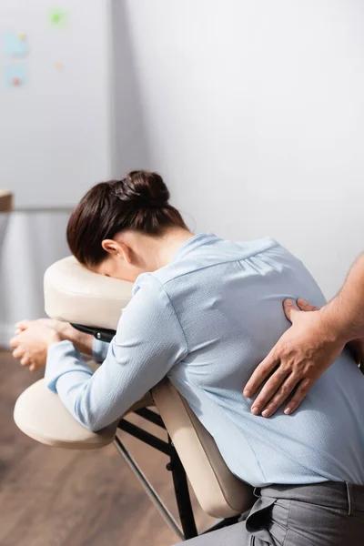 Masseur doing seated massage of back for female client on blurred background — Stock Photo