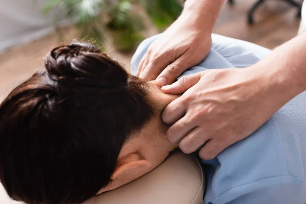 Vista de cerca de masajista haciendo masaje sentado de hombros enemigo morena mujer sobre fondo borroso - foto de stock