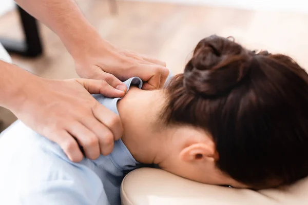 Close up view of masseur doing seated massage of neck for brunette woman on blurred background — Stock Photo