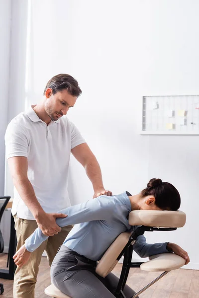 Сосредоточенный массажист делает сидячий массаж руки для брюнетки бизнес-леди в офисе — стоковое фото