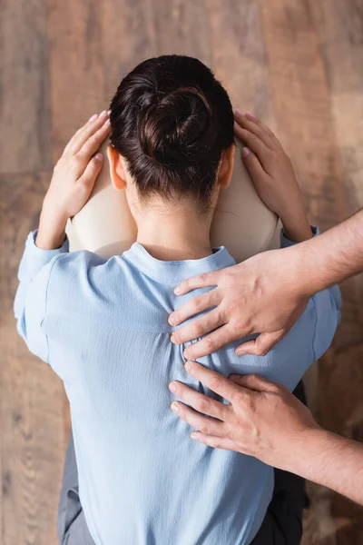 Vista dall'alto del massaggiatore che massaggia la schiena della donna d'affari bruna seduta sulla sedia da massaggio su sfondo strutturato — Foto stock