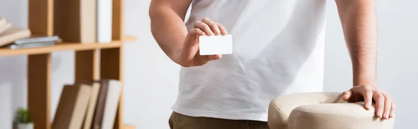 Vista cortada do massagista mostrando cartão de visita em branco, enquanto estava perto da cadeira de massagem no fundo borrado, banner — Fotografia de Stock