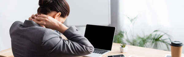 Back view of female office worker with hurting neck sitting at desk with laptop on blurred background, banner — Stock Photo