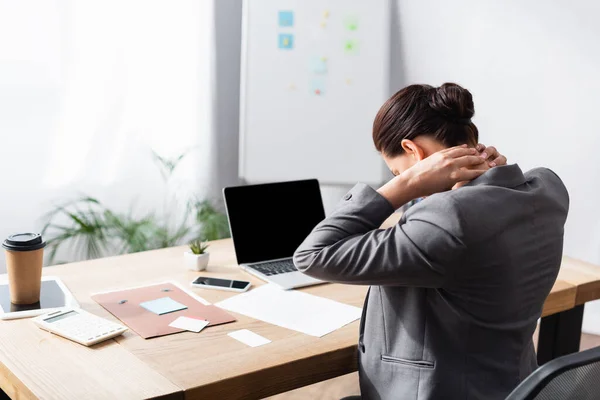 Empresária com dor no pescoço sentado no local de trabalho no escritório em fundo embaçado — Fotografia de Stock
