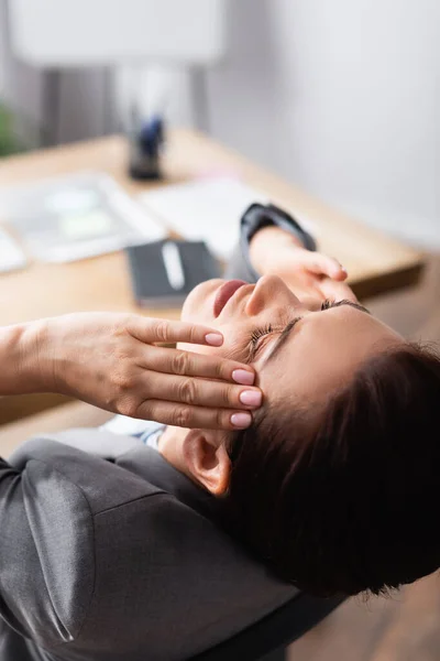 Vista de cerca de la mujer de negocios morena con dolor de cabeza con el lugar de trabajo borroso en el fondo - foto de stock