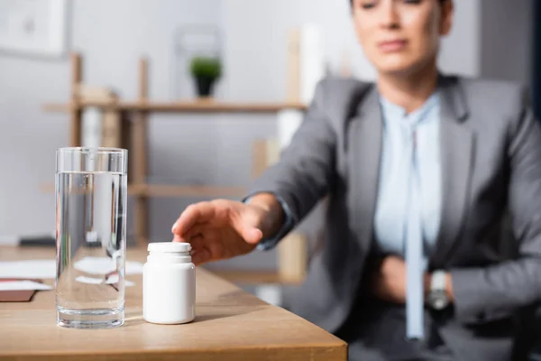 Ausgeschnittene Ansicht einer Geschäftsfrau mit Bauchschmerzen, die Medikamente auf verschwommenem Hintergrund einnimmt — Stockfoto