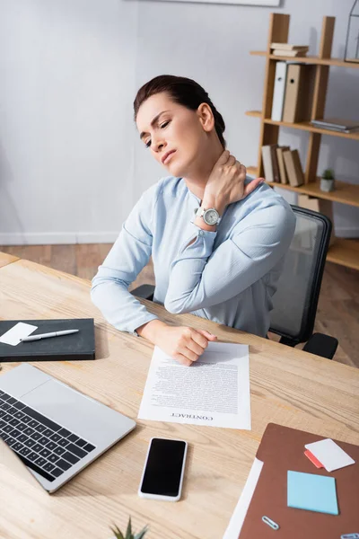Mujer de negocios con el cuello herido sentado en la silla de la oficina en el lugar de trabajo - foto de stock
