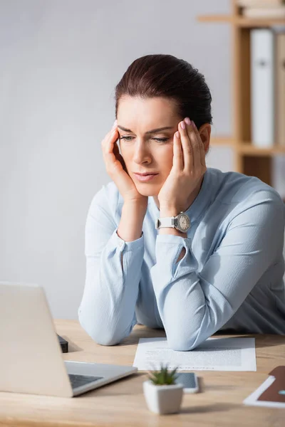 Müde brünette Geschäftsfrau mit Kopfschmerzen lehnt am Arbeitsplatz auf verschwommenem Hintergrund — Stockfoto