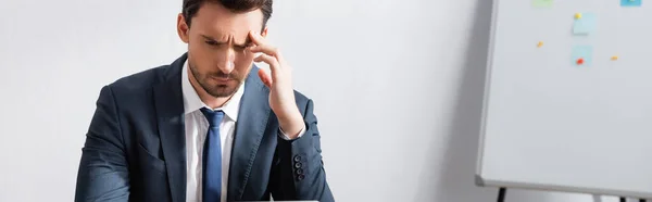 Müder Geschäftsmann mit Kopfschmerzen, die Hand in Tempelnähe haltend und mit verschwommenem Flipchart im Hintergrund wegschauend, Banner — Stockfoto