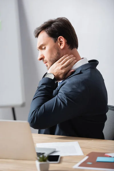 Seitenansicht eines Geschäftsmannes mit Nackenschmerzen am Arbeitsplatz auf verschwommenem Hintergrund — Stockfoto