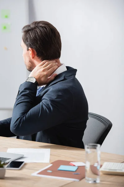 Büroangestellte mit schmerzhaftem Nacken sitzt am Arbeitsplatz vor verschwommenem Hintergrund — Stockfoto