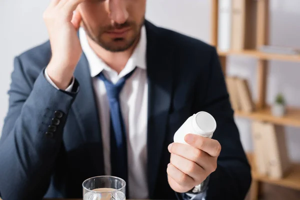 Vue recadrée d'un homme d'affaires tenant des médicaments près d'un verre d'eau sur fond flou — Photo de stock