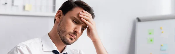 Hombre de negocios agotado con migraña agarrado de la mano en la frente, mientras mira hacia otro lado sobre un fondo borroso, pancarta - foto de stock