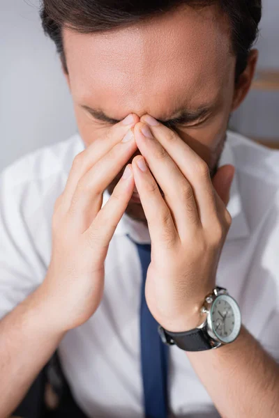 Close up view of tired businessman with headache, holding hands near closed eyes on blurred background — Stock Photo