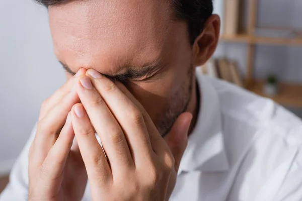 Close up view of exhausted office worker with migraine, holding hands near closed eyes on blurred background — Stock Photo