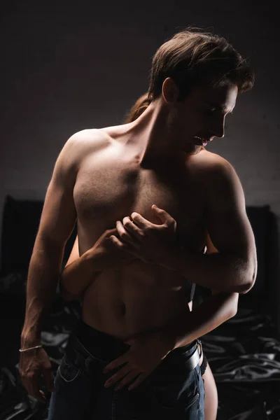 Женщина в трусиках обнимает мускулистого парня в спальне вечером — стоковое фото