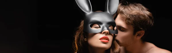 Shirtless man kissing sexy woman in rabbit mask with red lips isolated on black, banner — Stock Photo