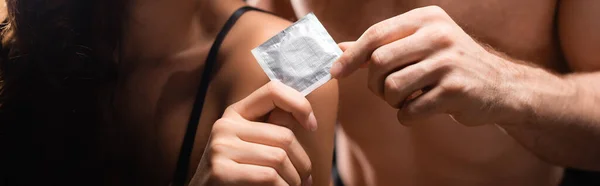 Cropped view of woman holding condom near shirtless man, banner — Stock Photo